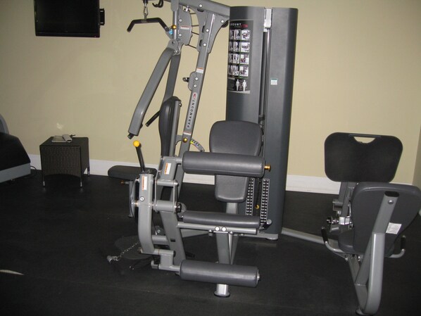 A gym with a weight machine, a bench, and a small table with a laptop. - The Atrium Resort (Providenciales)