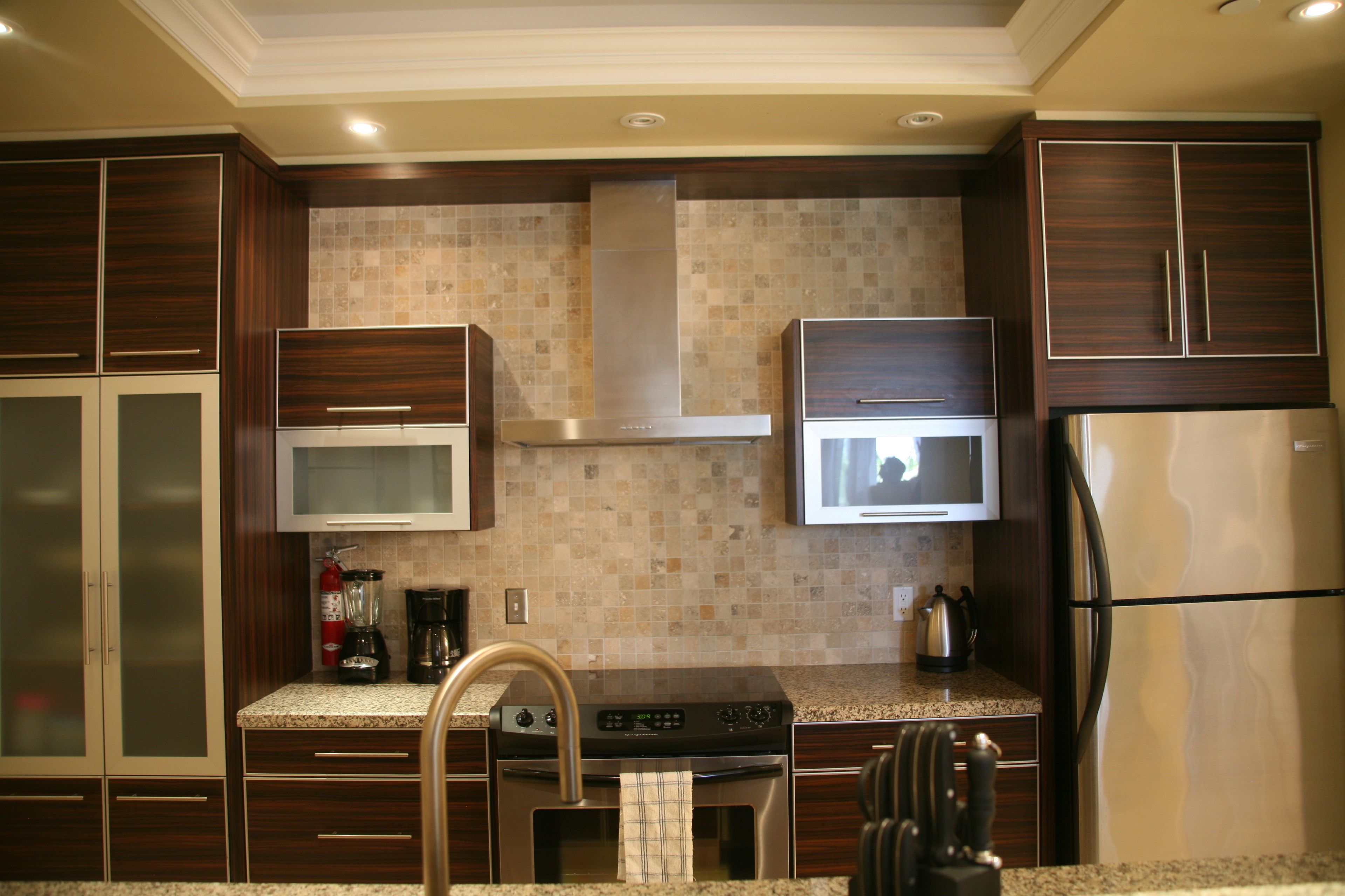 A modern kitchen with dark wood cabinets, stainless steel appliances, and a tiled backsplash.