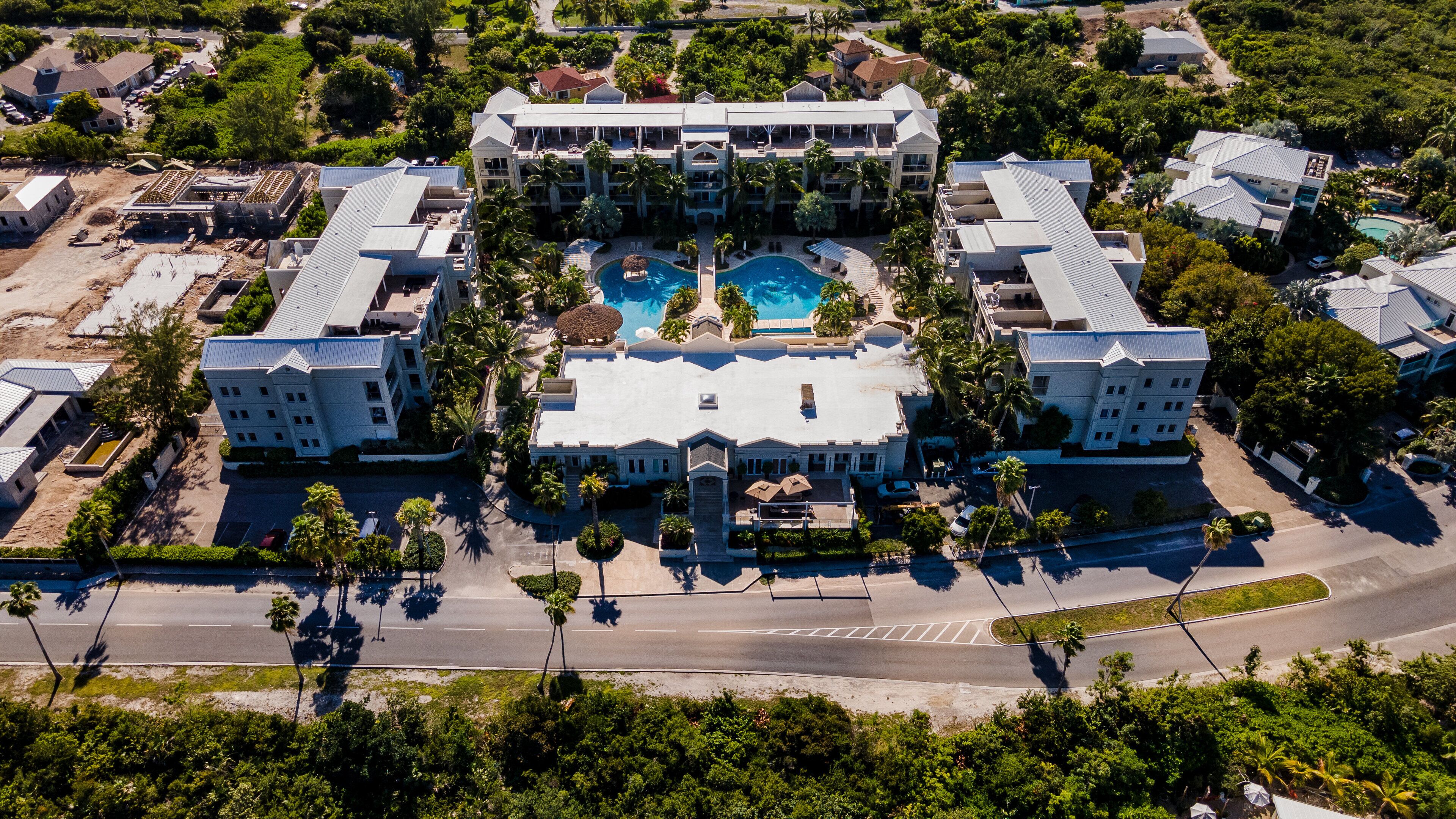 An aerial view of a resort with a central pool, multiple buildings, and palm trees.