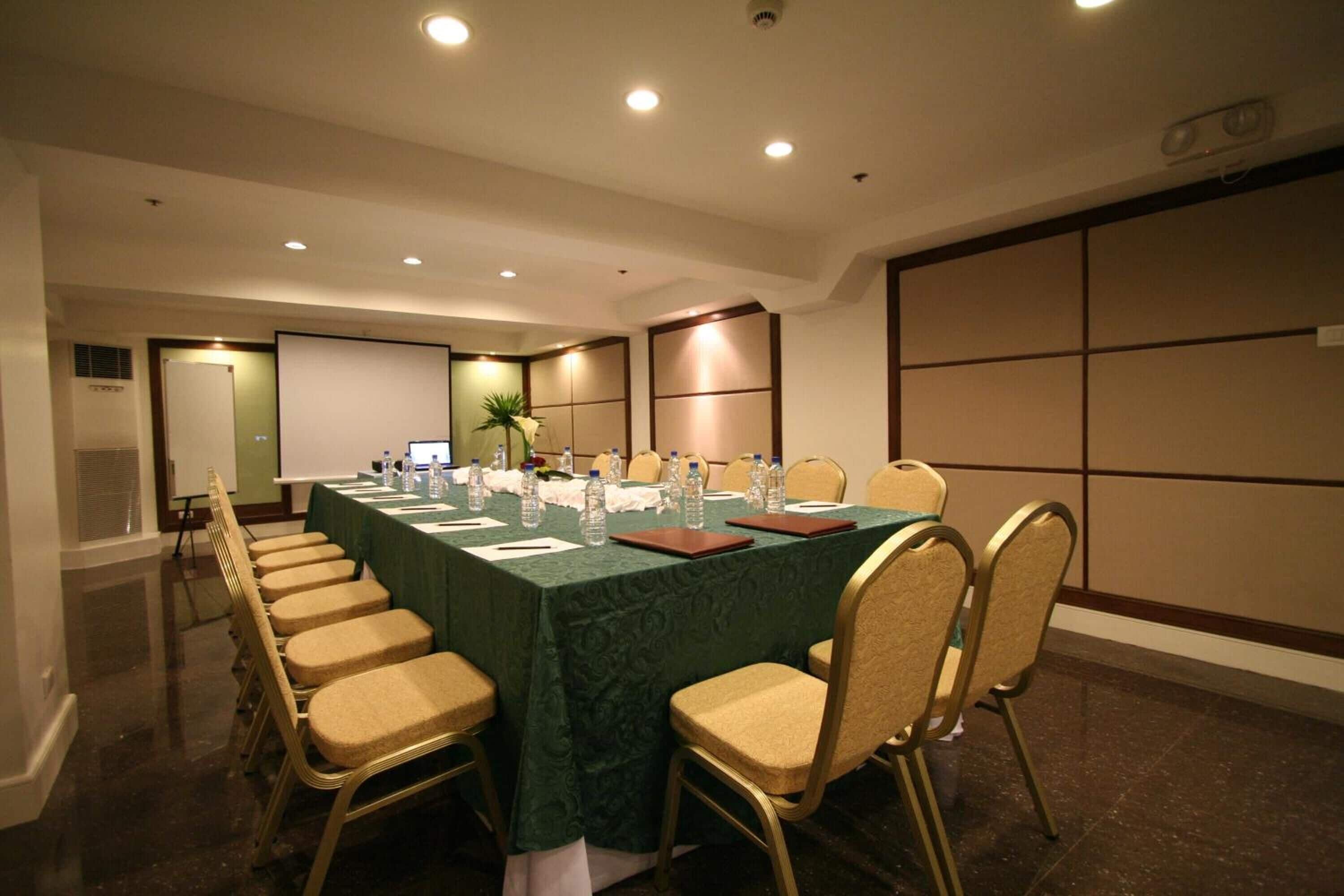 A conference room with a long table, chairs, and a projector screen.