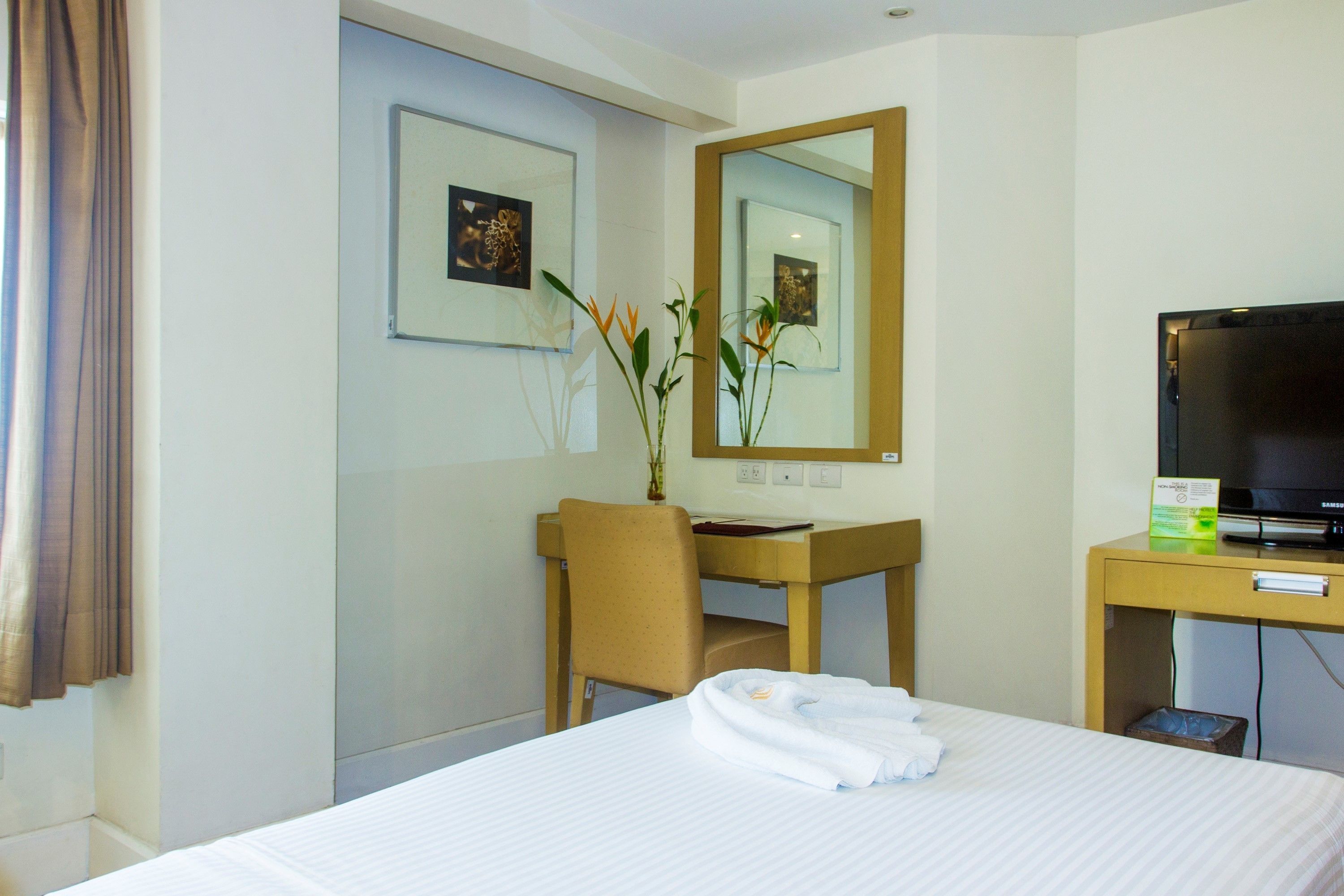 Una habitación de hotel con una cama, un escritorio, una silla, un televisor y un espejo.