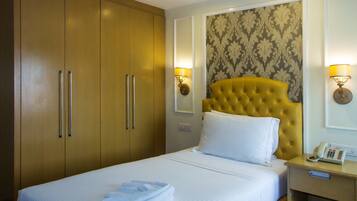 A hotel room with a bed, a yellow headboard, a bedside table with a phone, and a wardrobe with two doors.