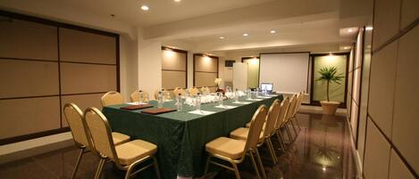 Una sala de conferencias con una larga mesa, sillas y una pantalla para proyector.