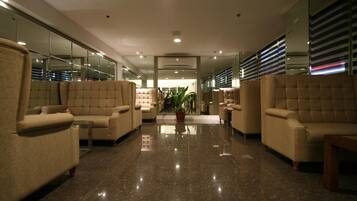 A lobby with plush seating, a central plant, and a mirrored wall.