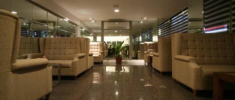 A lobby with plush seating, a central plant, and a mirrored wall.