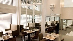 A modern dining area with tables and chairs, a chandelier, and large windows with blinds. - Hotel St Ellis (Legazpi)