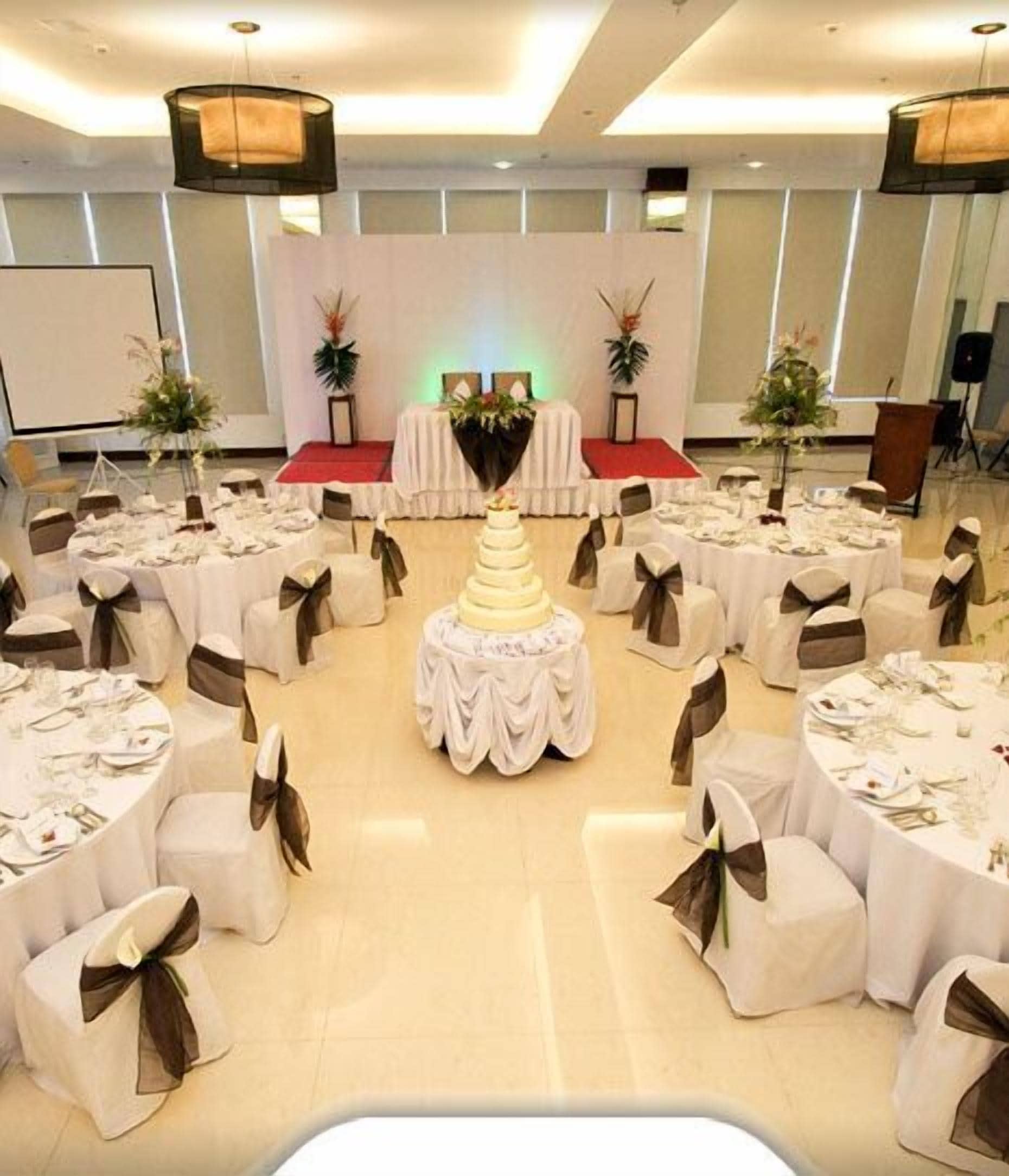 Een balzaal met ronde tafels gedekt voor een formeel evenement, een podium en een grote bloemstuk in het midden.