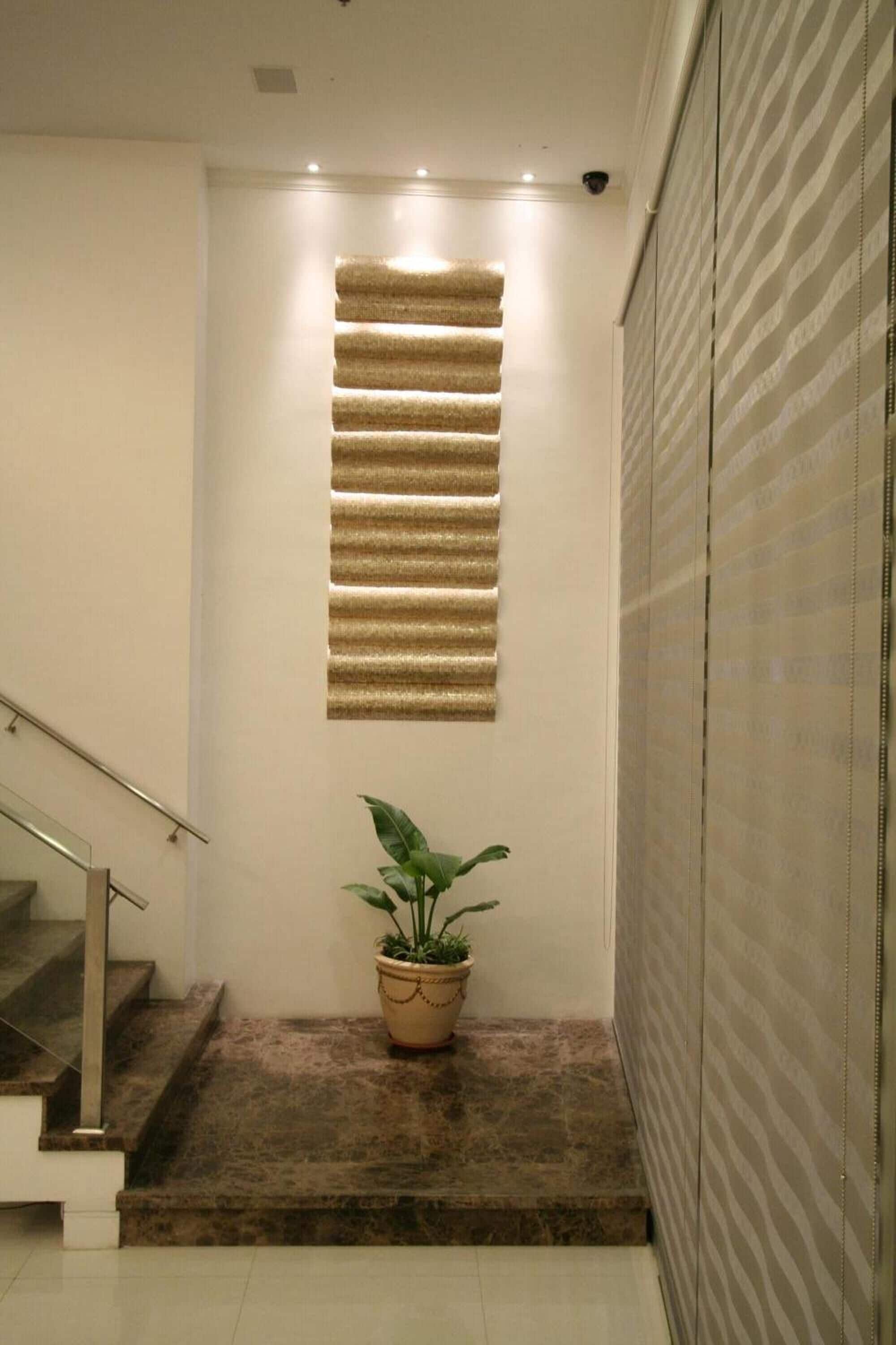 A staircase with a potted plant at the bottom, a wall-mounted light fixture, and a security camera on the ceiling.