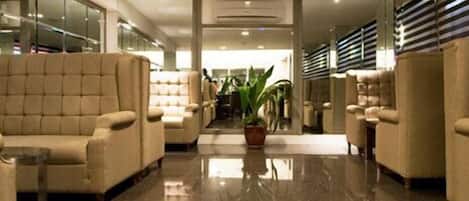 A lobby with a polished marble floor, beige upholstered chairs, and a central potted plant.