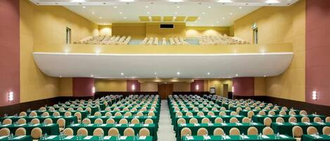 A conference room with rows of tables and chairs, a balcony with seating, and a stage area.