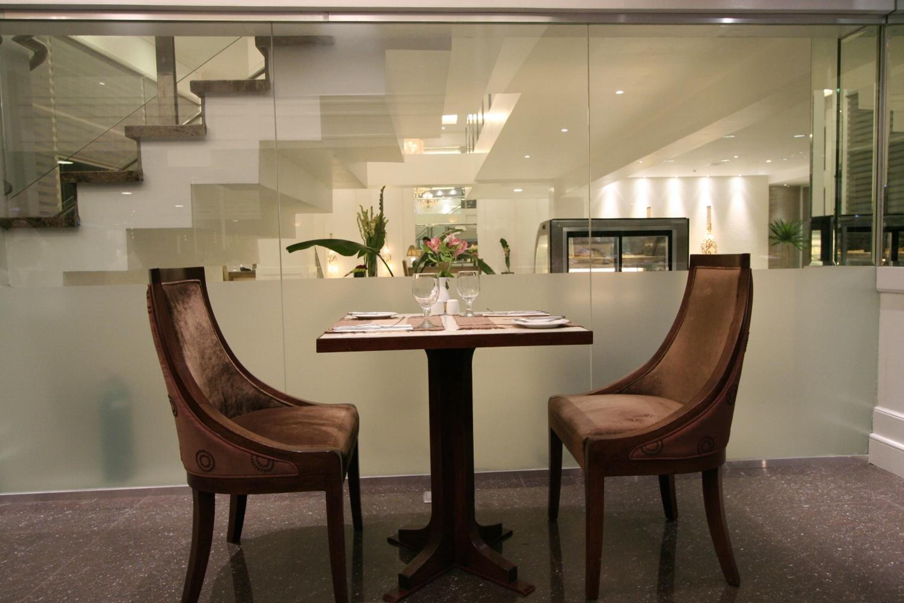 Un coin repas avec une table dressée pour deux personnes, deux chaises rembourrées et un vase rempli de fleurs.