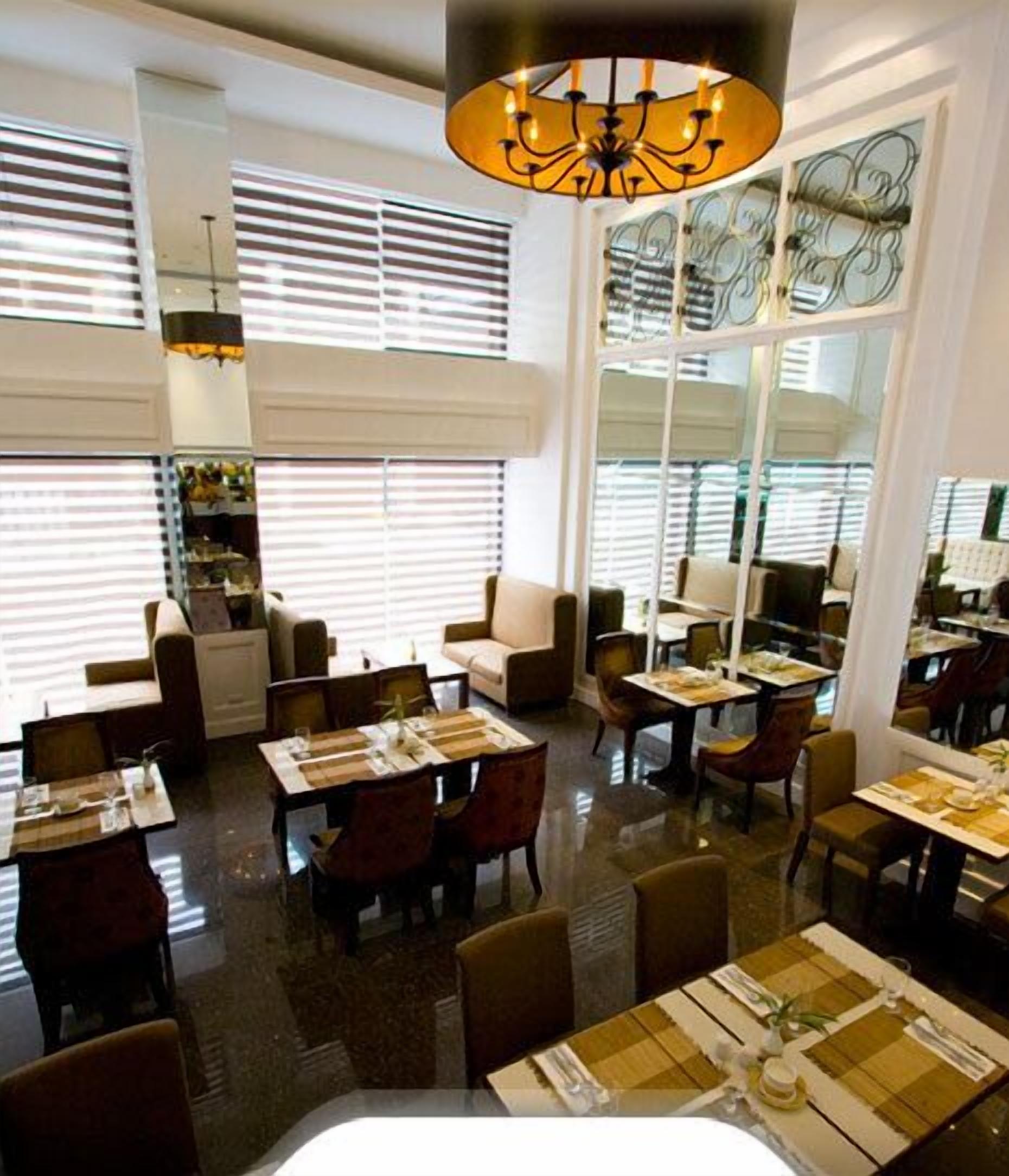 A restaurant with multiple dining tables and chairs, large windows with blinds, and a chandelier.