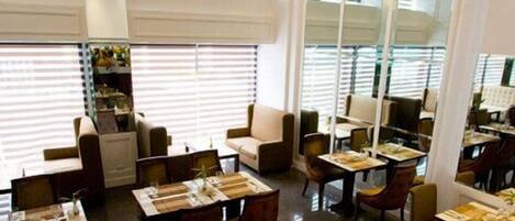 A restaurant with multiple dining tables and chairs, large windows with blinds, and a chandelier.