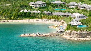 A coastal resort with multiple bungalow-style buildings, a sandy beach, and a rocky shoreline.