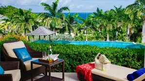 A poolside area with wicker furniture, a table with a bottle and glasses, and a view of the ocean and palm trees.