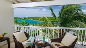 A balcony with wicker furniture, a small table, and a view of a tropical beach and ocean.