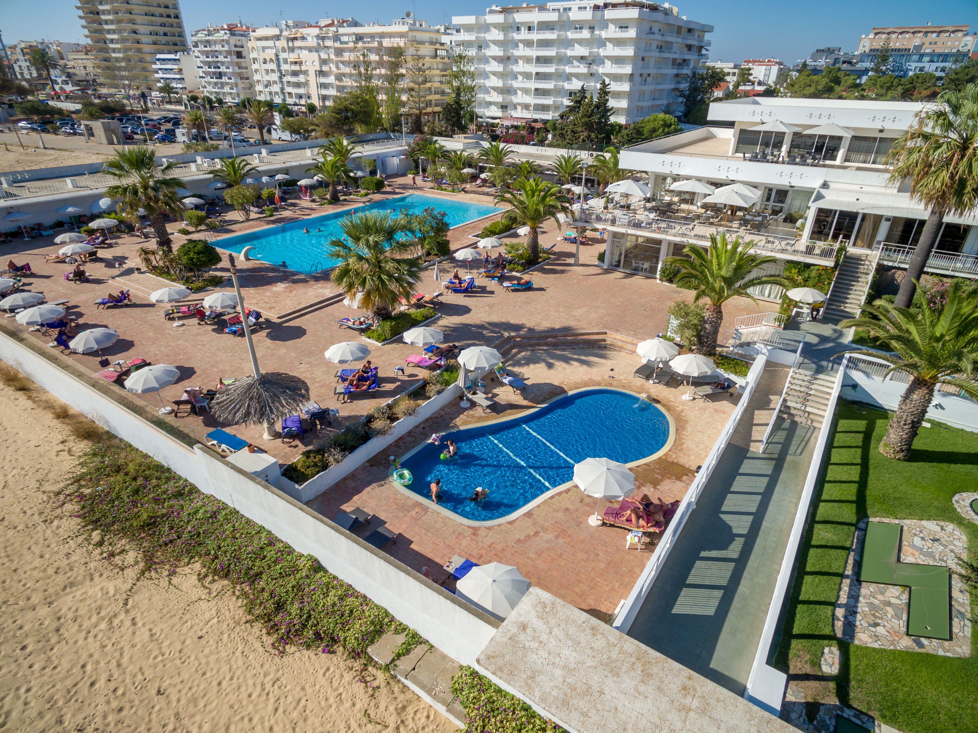 A resort with a large pool, sun loungers, umbrellas, and a view of the city.