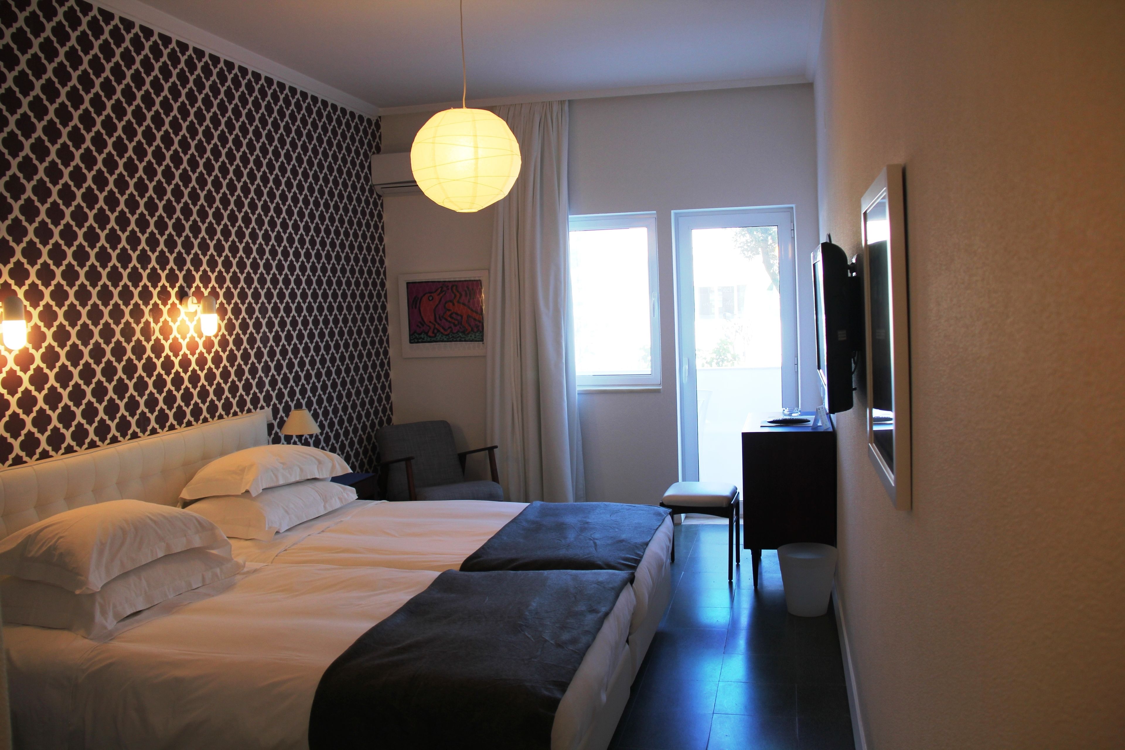 Une chambre d’hôtel avec un lit, un bureau, une chaise, une lampe et une fenêtre.