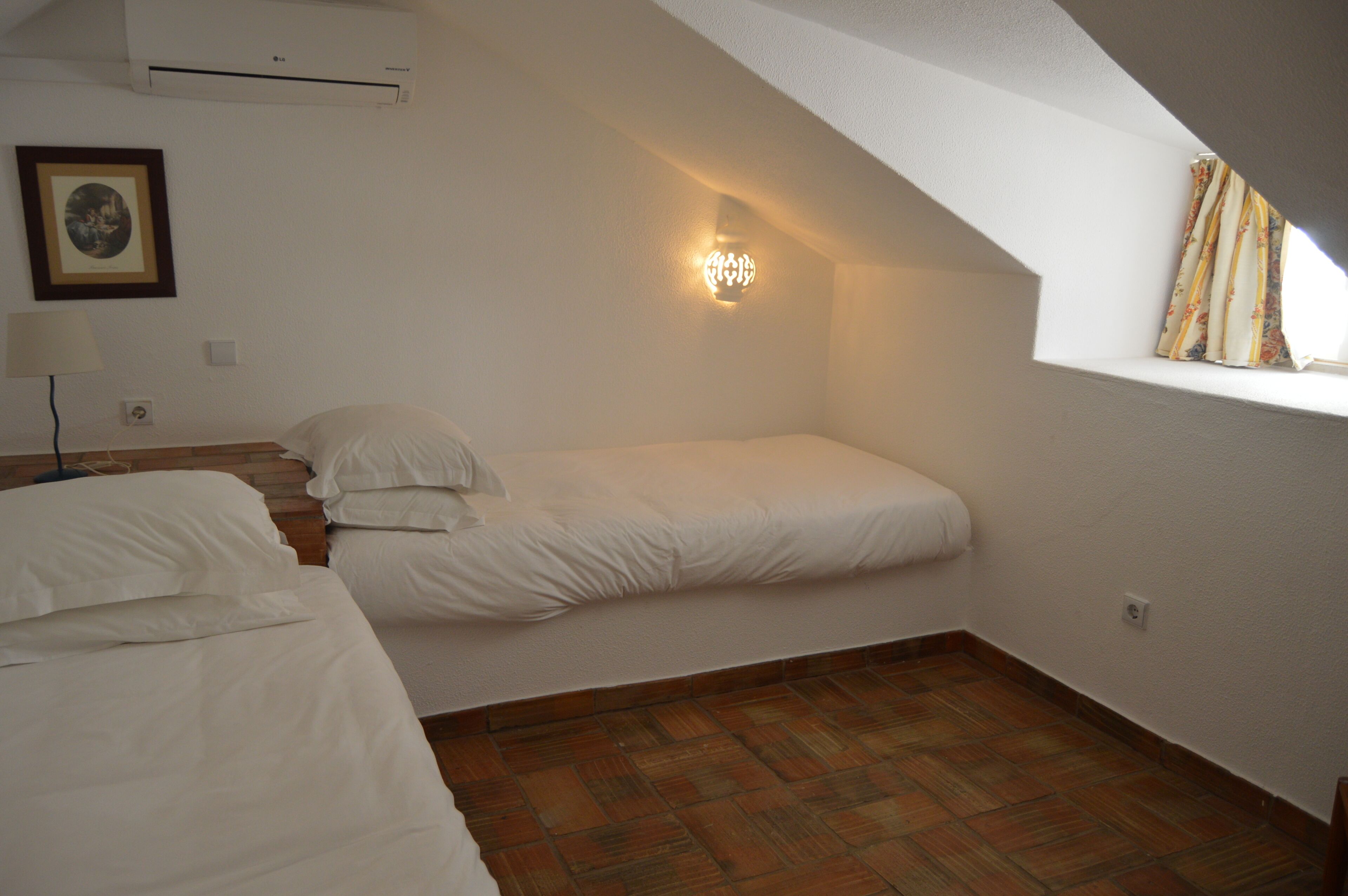 Una habitación pequeña y acogedora con techo inclinado, una cama individual, una lámpara de noche y una lámpara de pared.