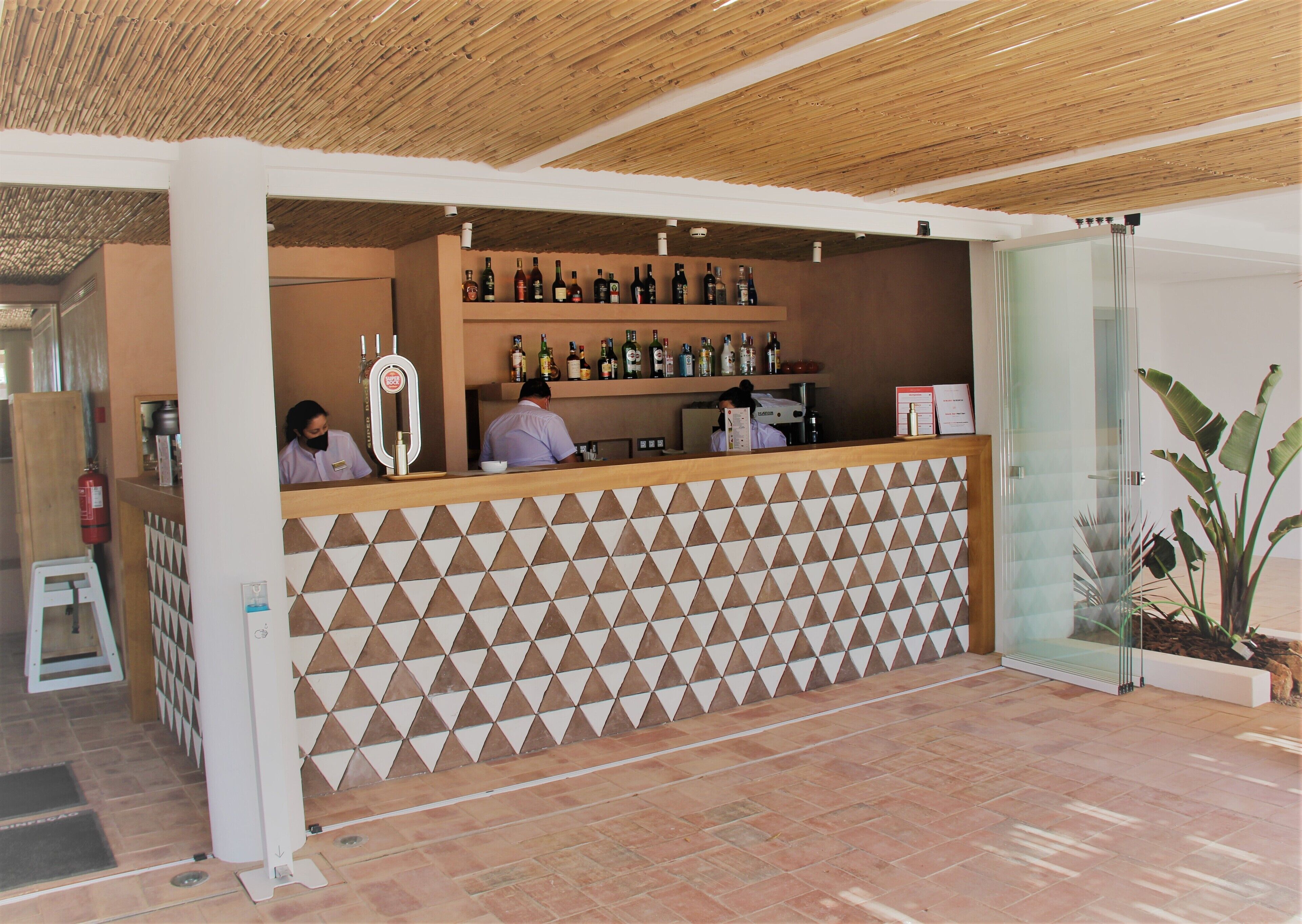A bar area with a geometric patterned wall, shelves with bottles, and a counter with staff.