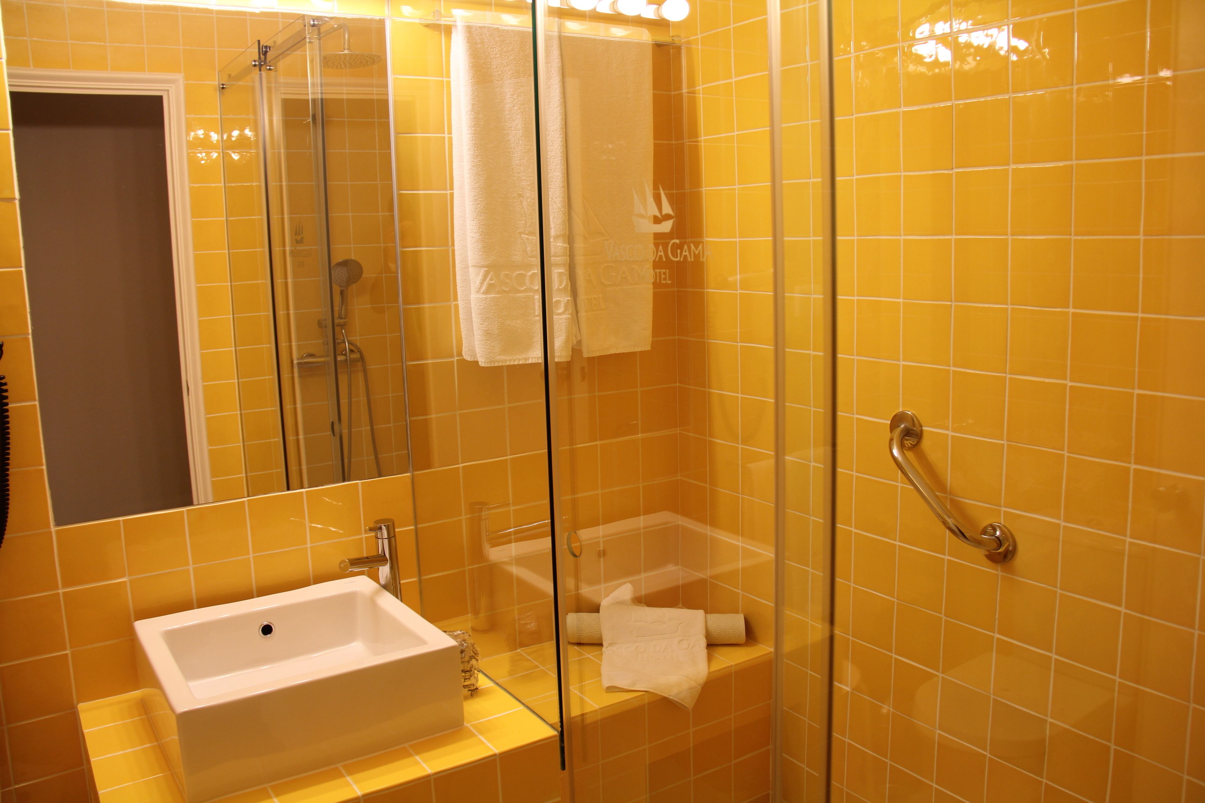 Un baño con ducha vidriada, lavamanos y un perchero para toallas.