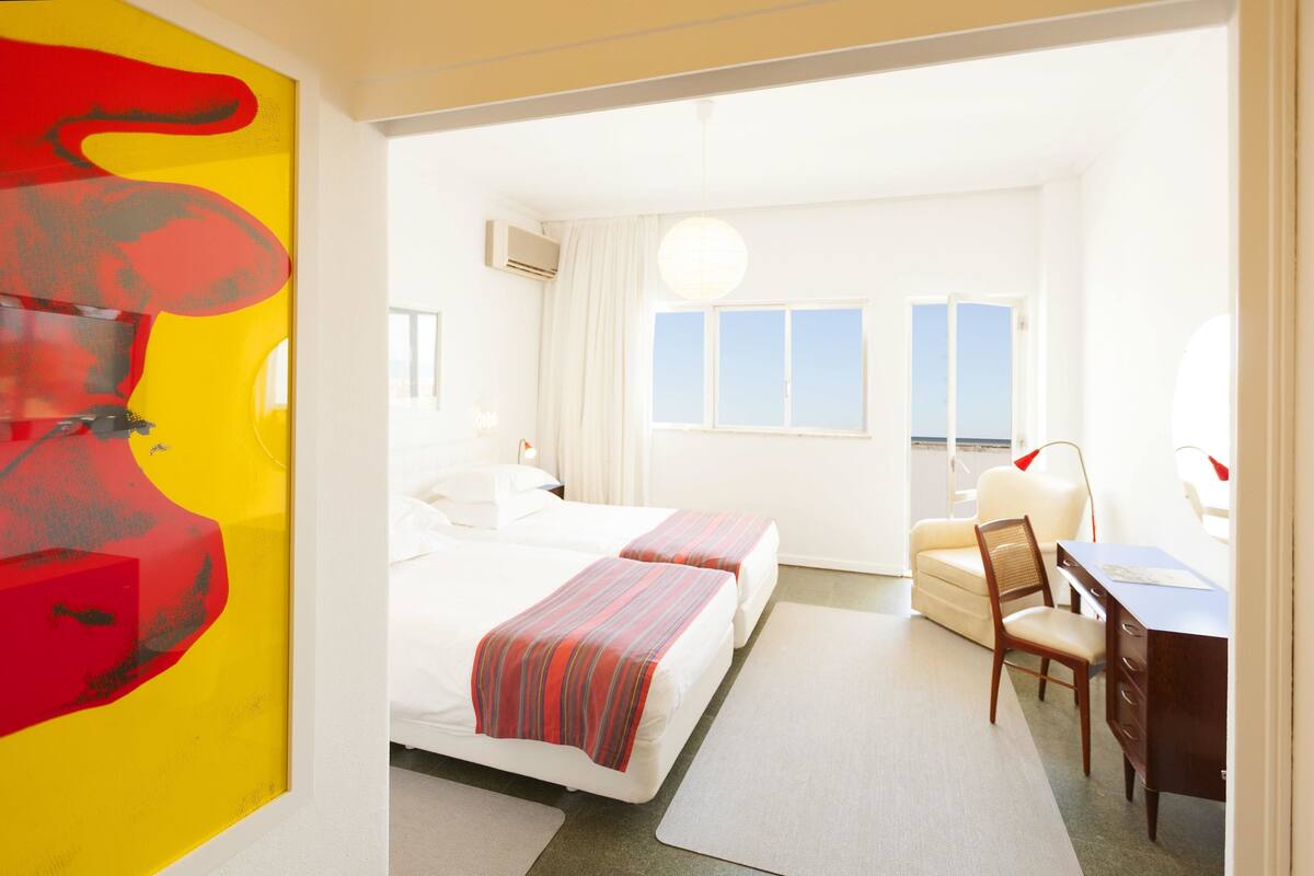A hotel room with two beds, a desk, a chair, and a large abstract painting on the wall.