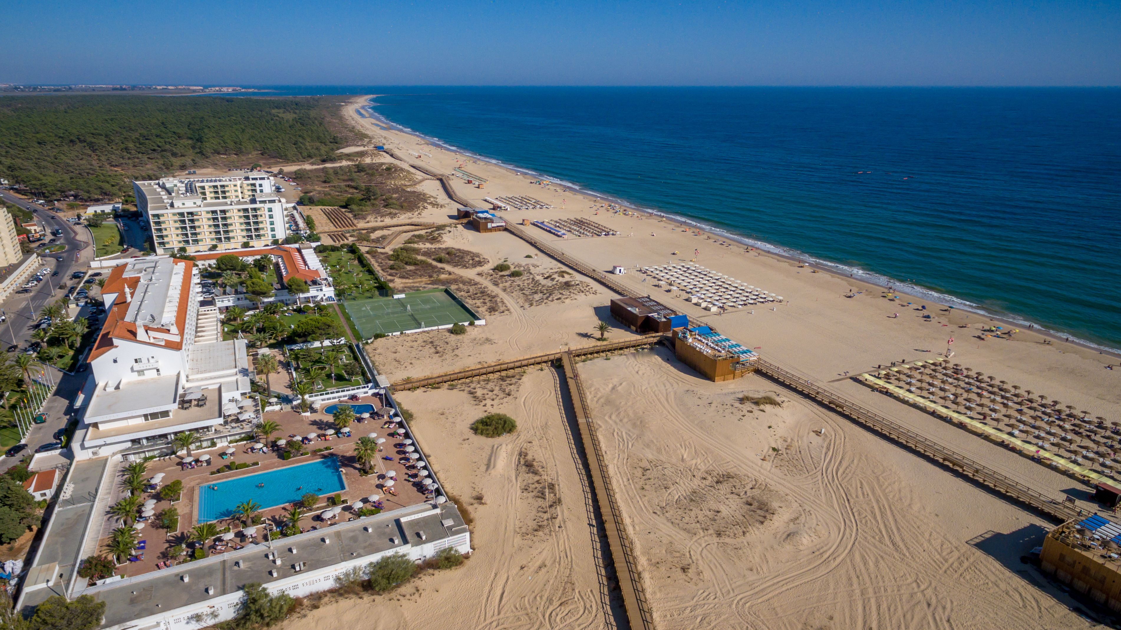 Vista aérea de un hotel frente al mar con piscina, zona de playa y un muelle largo.