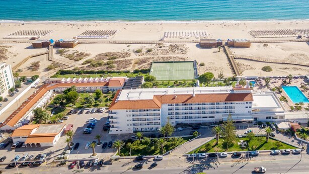 An aerial view of a coastal hotel with a large building, a tennis court, a swimming pool, and a beach area. - Vasco da Gama Hotel (Vila Real Santo Antonio)