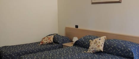 Una habitación con dos camas individuales, cada una con una colcha estampada y almohadas a juego. Hay una mesita de noche pequeña con una lámpara y un cuadro enmarcado en la pared sobre las camas.