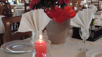 Une table à manger avec une bougie, un vase rempli de fleurs rouges et un chandelier en verre.