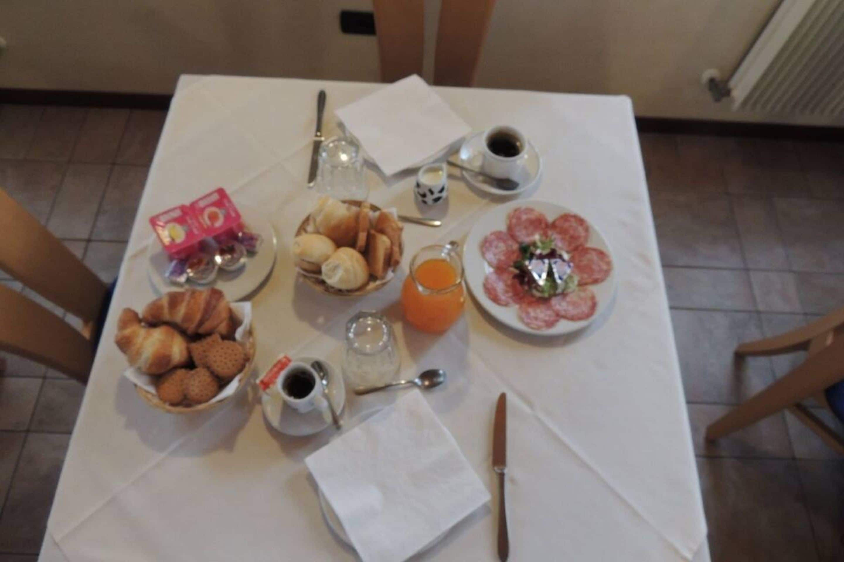 A breakfast table with croissants, pastries, a plate of salami, orange juice, and coffee.