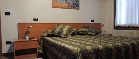 A bedroom with a bed, nightstands, a lamp, a painting on the wall, and a window with curtains.