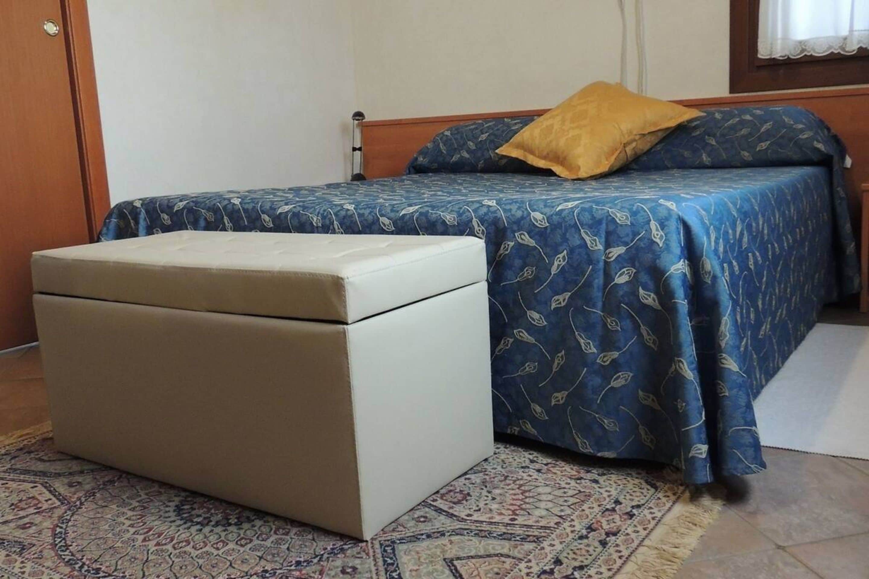 Een klein, netjes opgemaakt bed met een blauw gebloemd beddegoed en één geel kussen.