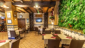 A restaurant with tiled floors, wooden beams, and a green wall with plants. Tables and chairs are neatly arranged. - Hotel Pacoche Murcia (Murcia)