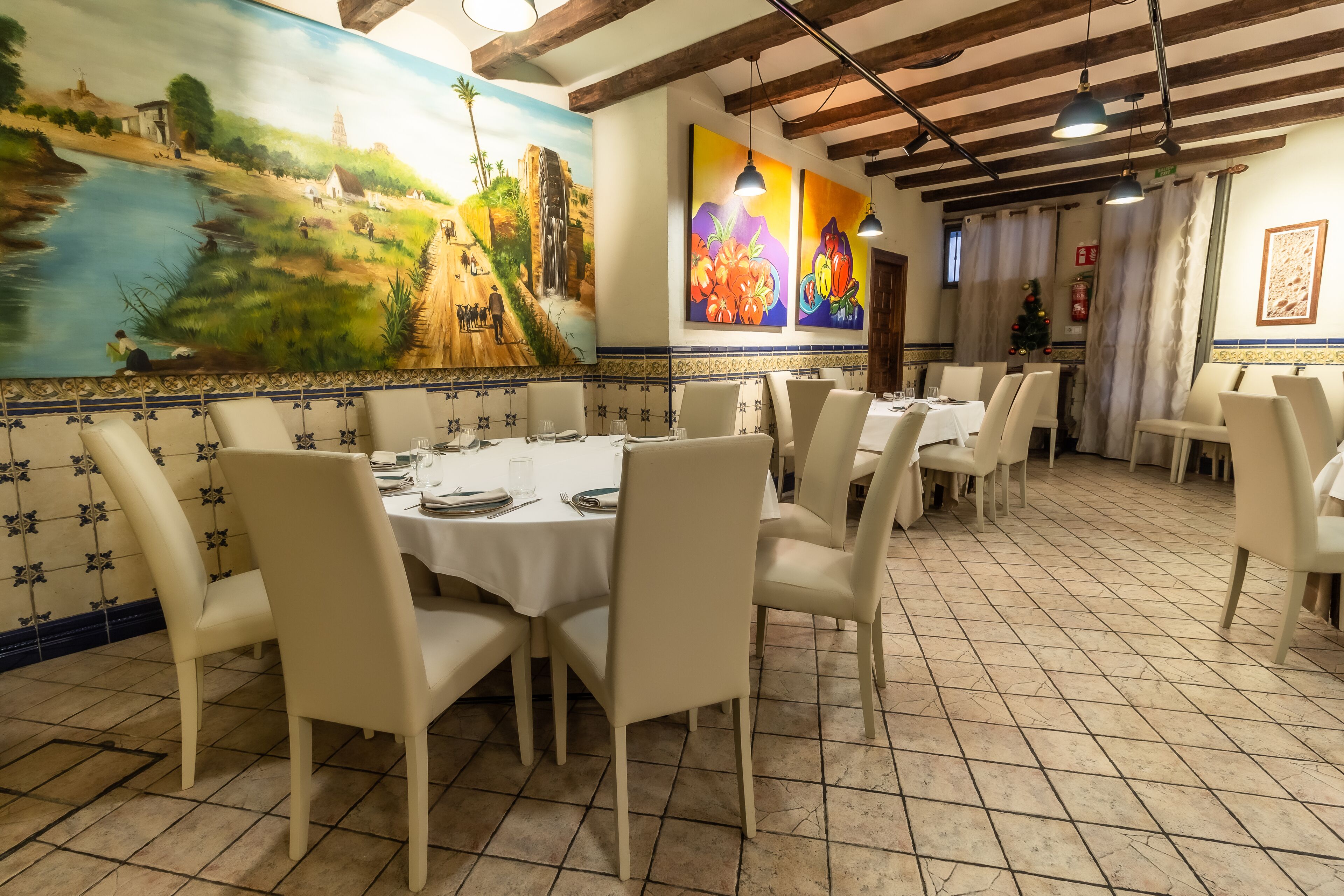 Un restaurante con un mural de un paisaje, paredes y piso de baldosas.