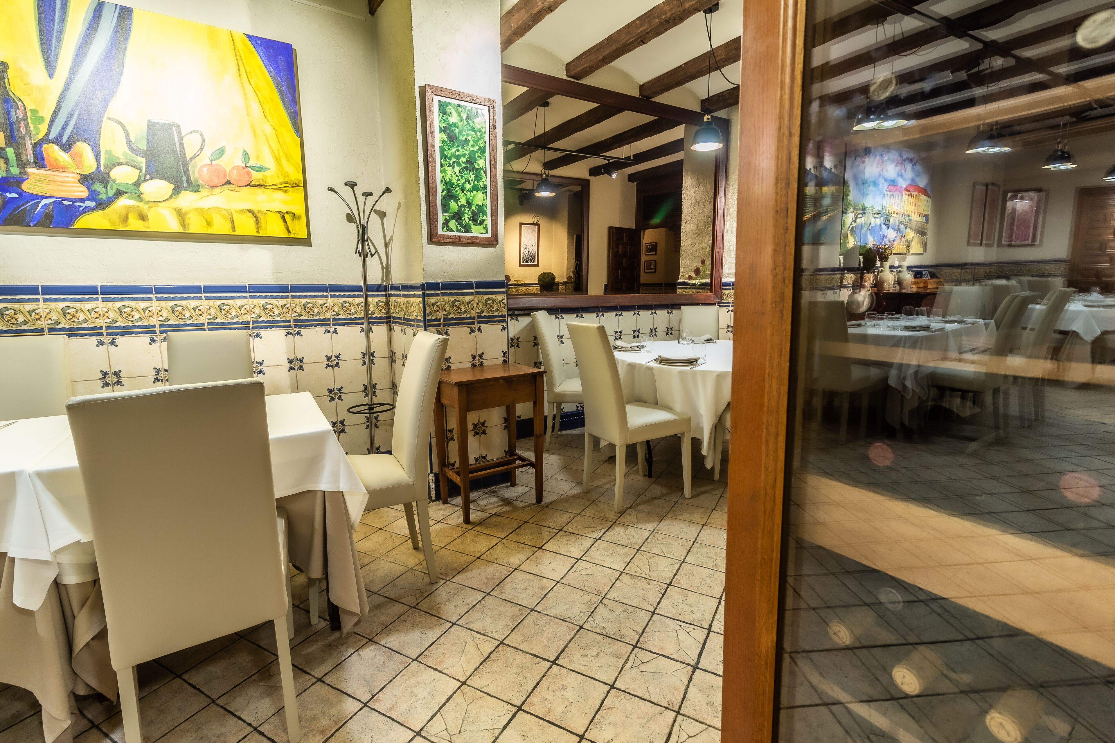 Un restaurante con mesas y sillas blancas, suelo de baldosas y obras de arte en las paredes.