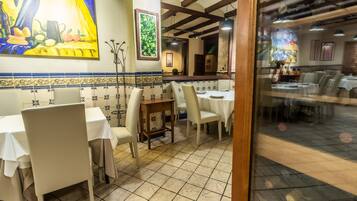 Un restaurante con mesas y sillas blancas, suelo de baldosas y obras de arte en las paredes.