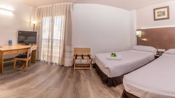 A hotel room with a desk, two beds, a TV, and a window with curtains.