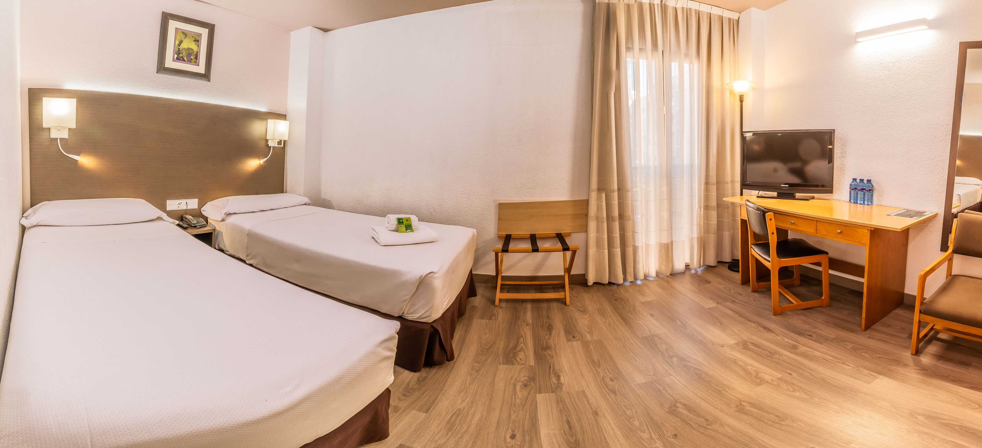 A hotel room with two beds, a desk with a chair, a television, and a small table.