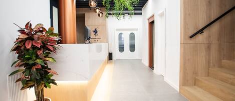 A modern reception area with a potted plant, a wooden reception desk, and a staircase.