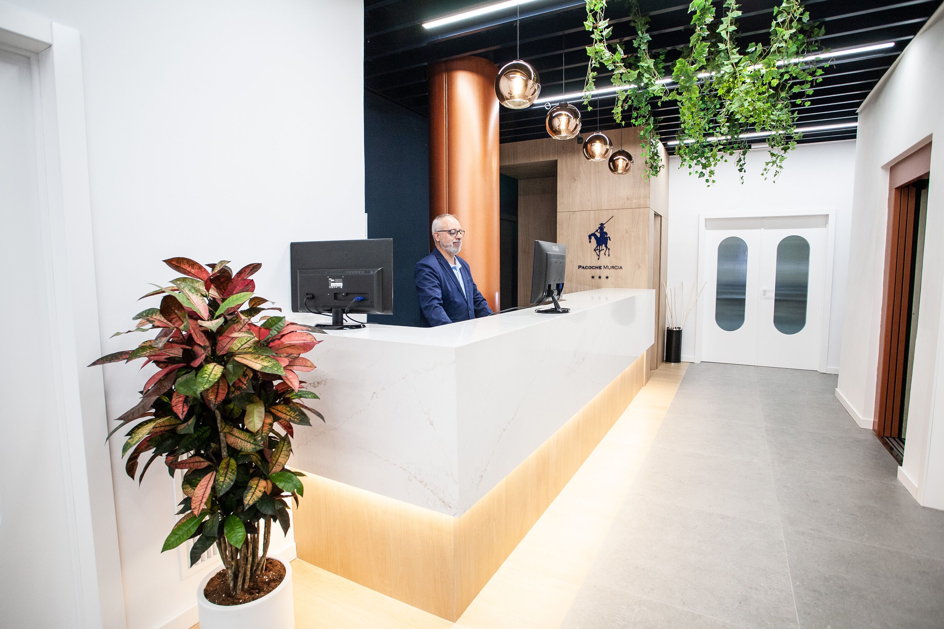 A reception desk with a modern design, a potted plant, and a logo on the wall.