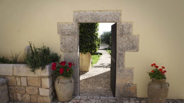 A stone archway leading to a pathway, with two large vases of red flowers on either side. - Villa Teresa Resort (Modica)