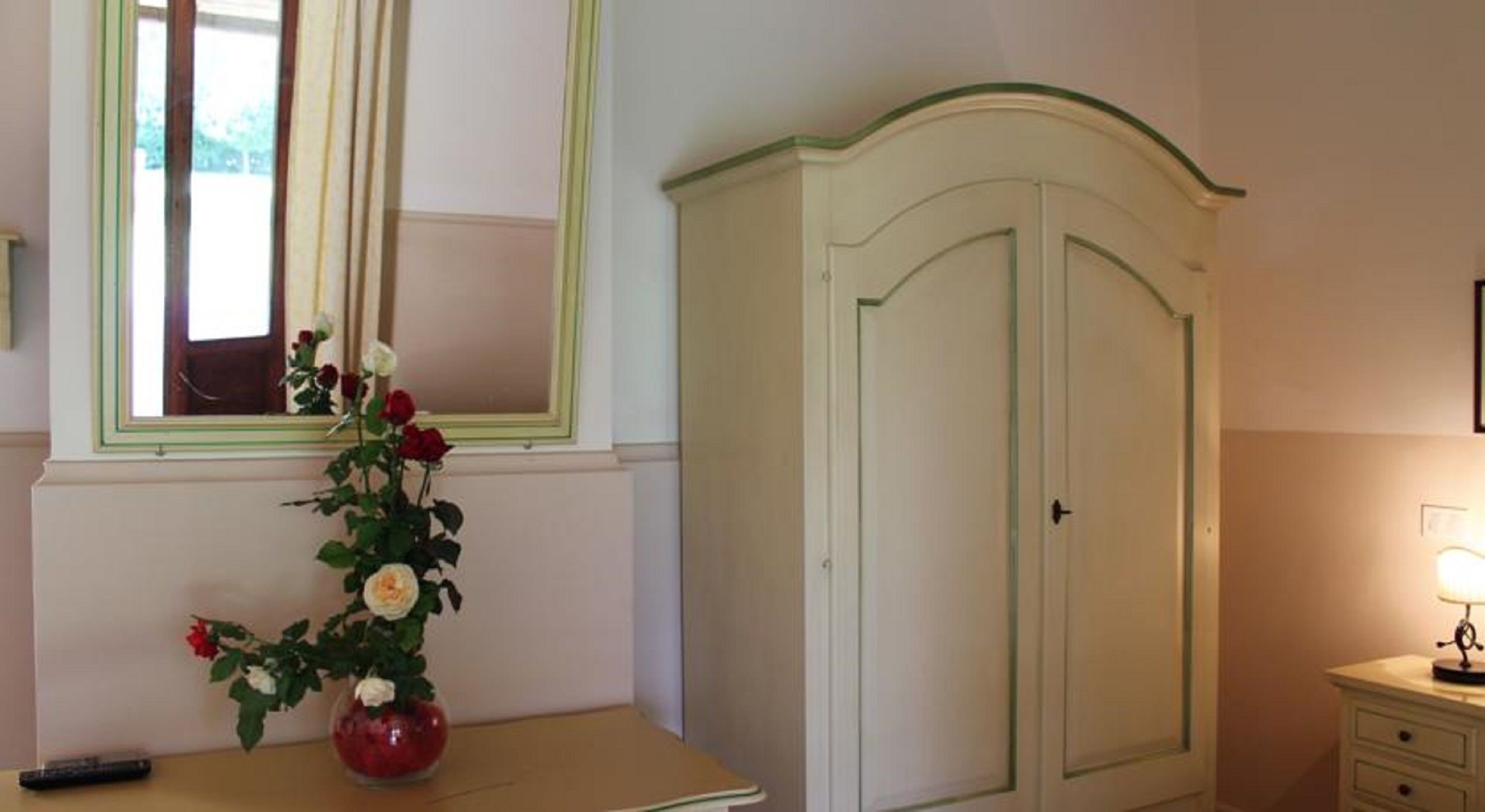 A room with a bed, a bedside table with a vase of flowers, a window with curtains, and a wardrobe.