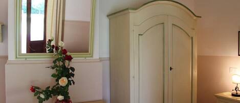 A room with a bed, a bedside table with a vase of flowers, a window with curtains, and a wardrobe.