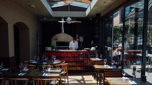 An indoor dining area with wooden tables and chairs, a central kitchen with a chef, and large windows allowing natural light. - The Kings Arms (Berkhamsted)