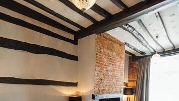 A room with exposed wooden beams, a brick fireplace, and a large window with curtains.
