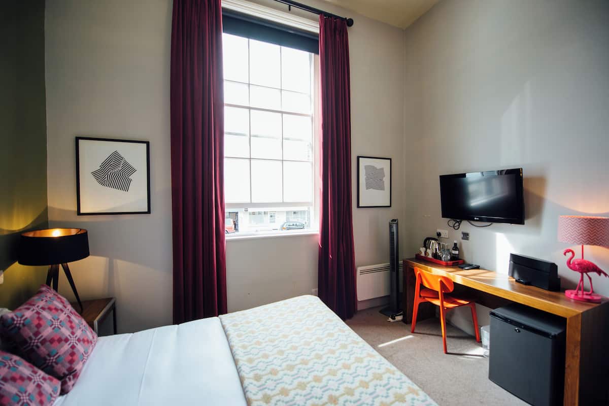 A hotel room with a bed, a desk with a computer, a television, and a window with curtains.