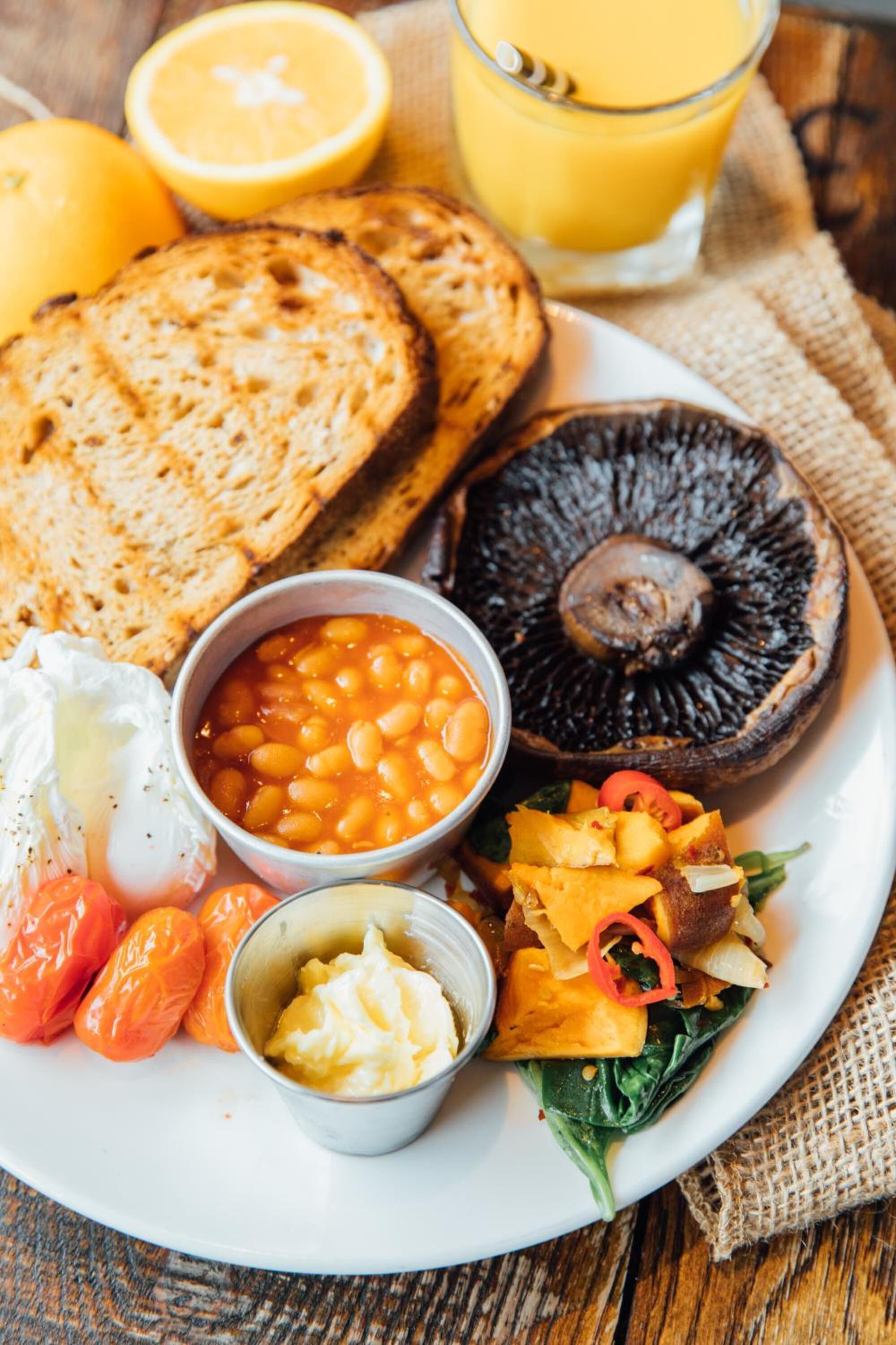 A plate with toast, beans, a mushroom, eggs, tomatoes, and a glass of orange juice.