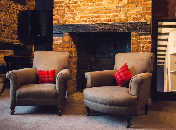 Two armchairs with red patterned cushions in front of a brick wall and a fireplace. - The Kings Arms (Berkhamsted)