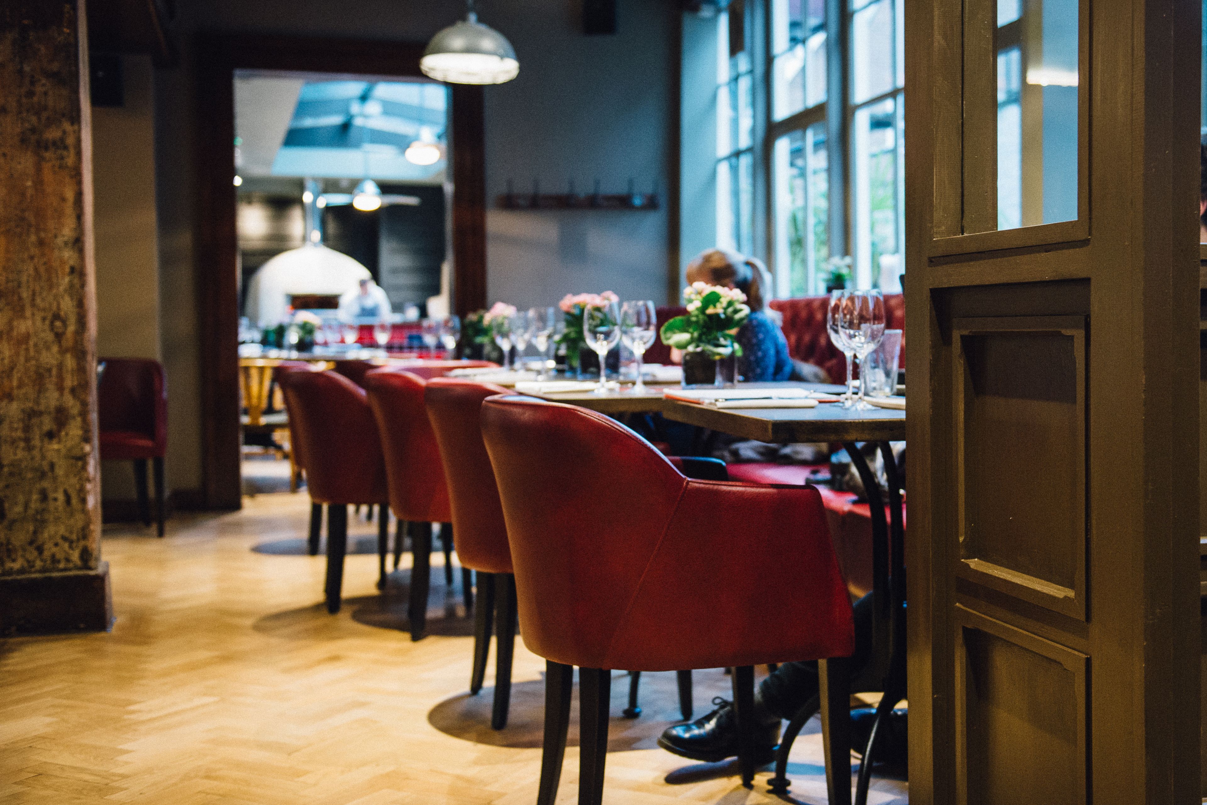 A restaurant interior with wooden flooring, red upholstered chairs, and tables set for dining.